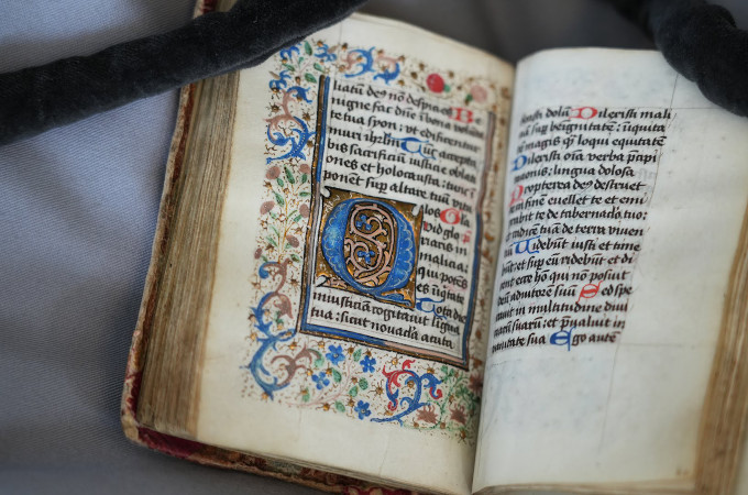 Psalterium feriatum opengeklapt, waarbij links een kleurrijk opgemaakte bladzijde te zien is met wat lijkt latijns schrift. De rechter pagina is alleen tekst, met zoals het lijkt rode en blauwe hoofdletters aan het begin van iedere zin.